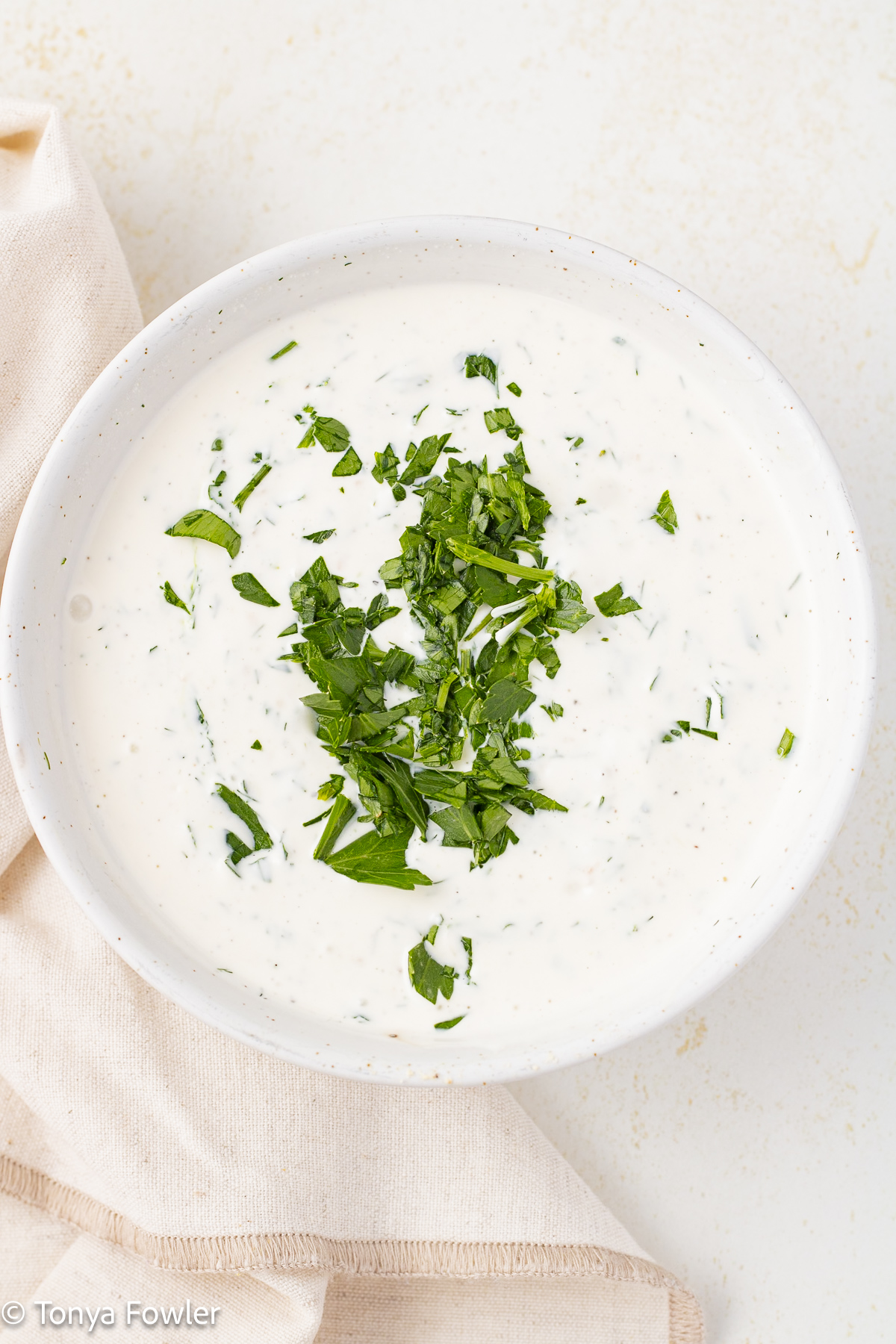 Close up image of a dipping sauce in a bowl with fresh herbs on top.