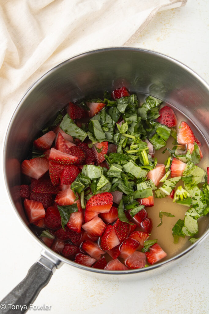 Chopped strawberries, basil and sugar in a sauce pot.
