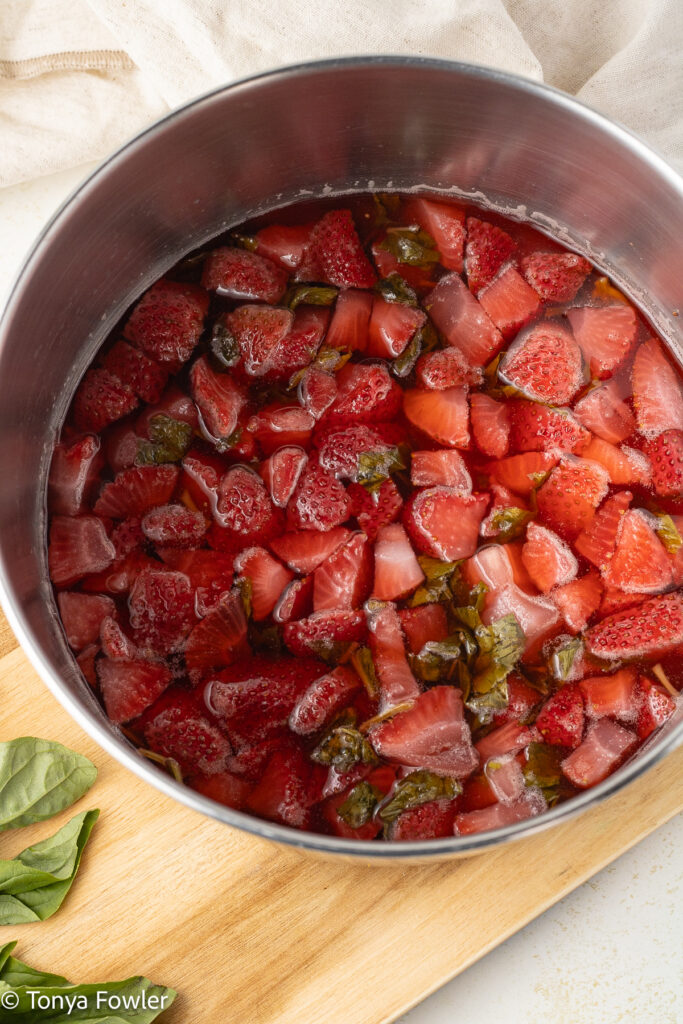 Cooked strawberries and basil in a sauce pot.