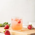 Straight on view of a strawberry basil mocktail sitting on a cutting board surrounded by fresh strawberries.