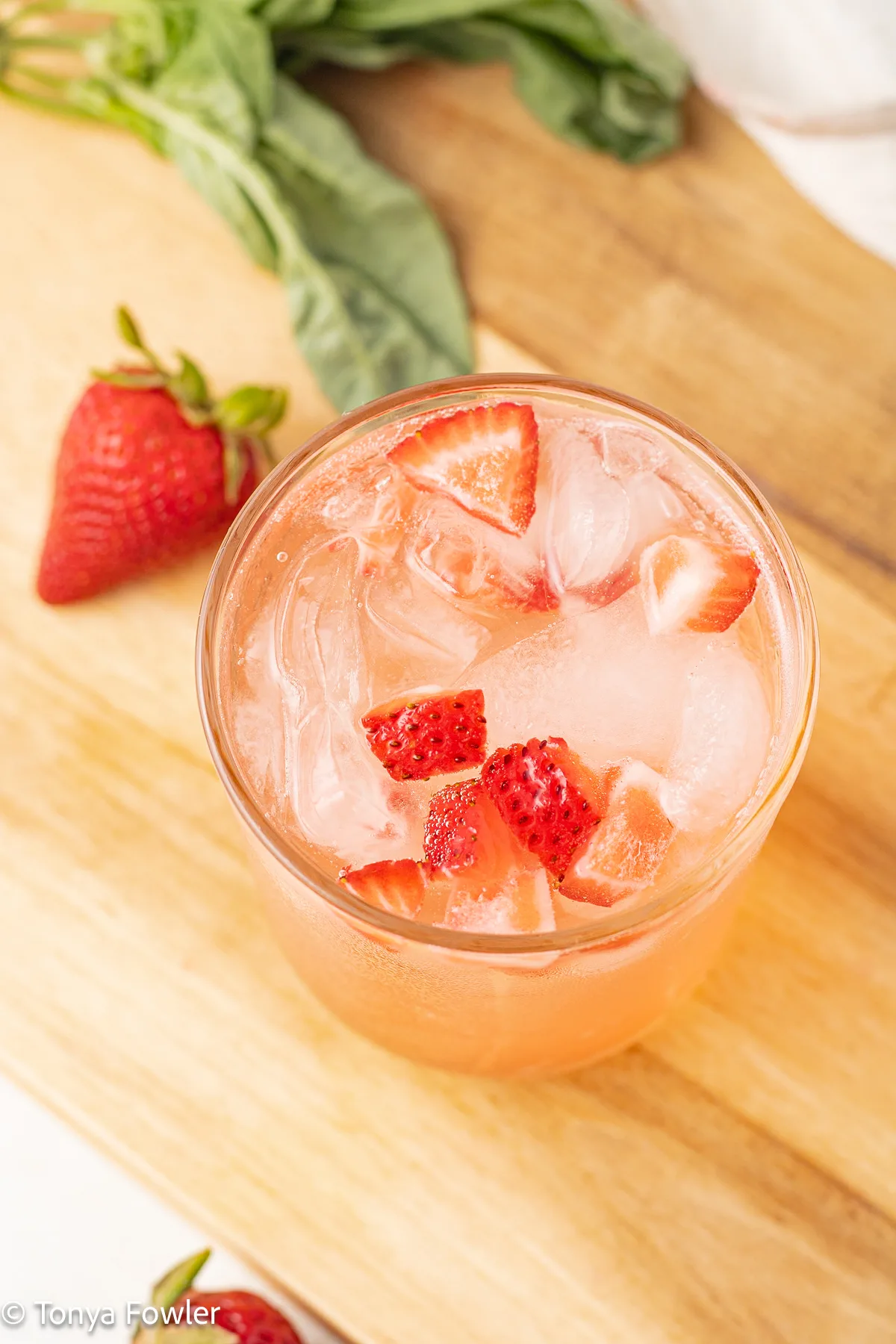 3/4 view of a strawberry mocktail in a glass with chopped strawberries.