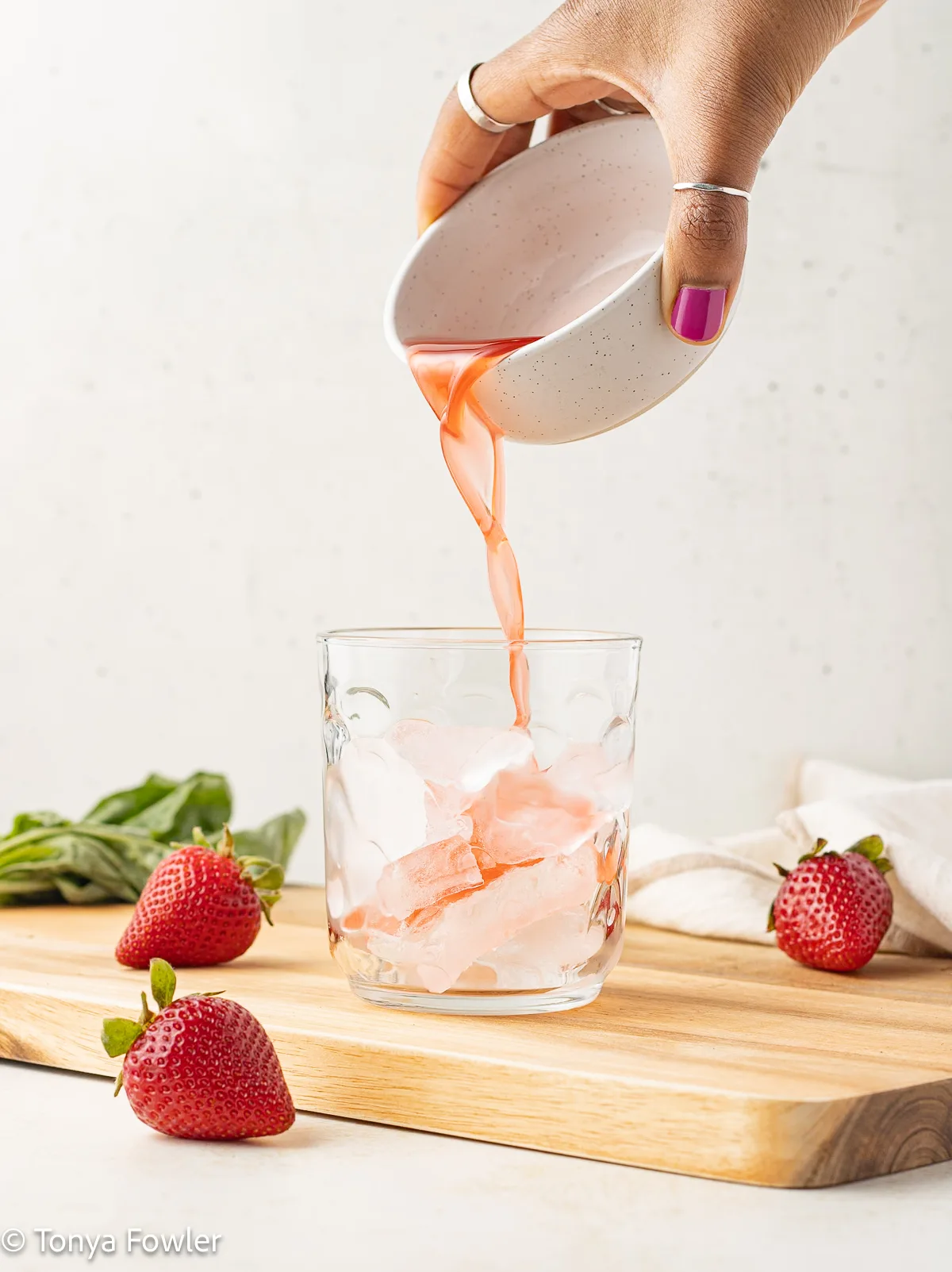 Hand pouring syrup into a glass with ice.