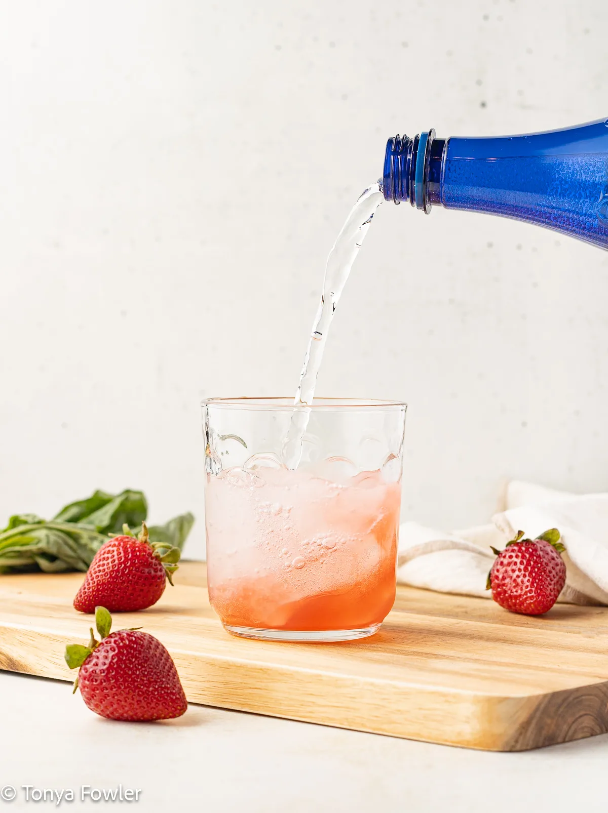 Sparkling water being poured in a glass with syrup.
