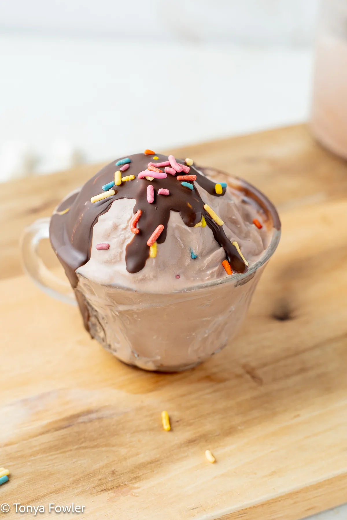 Scoop of chocolate protein ice cream in a glass topped with sprinkles and chocolate sauce.