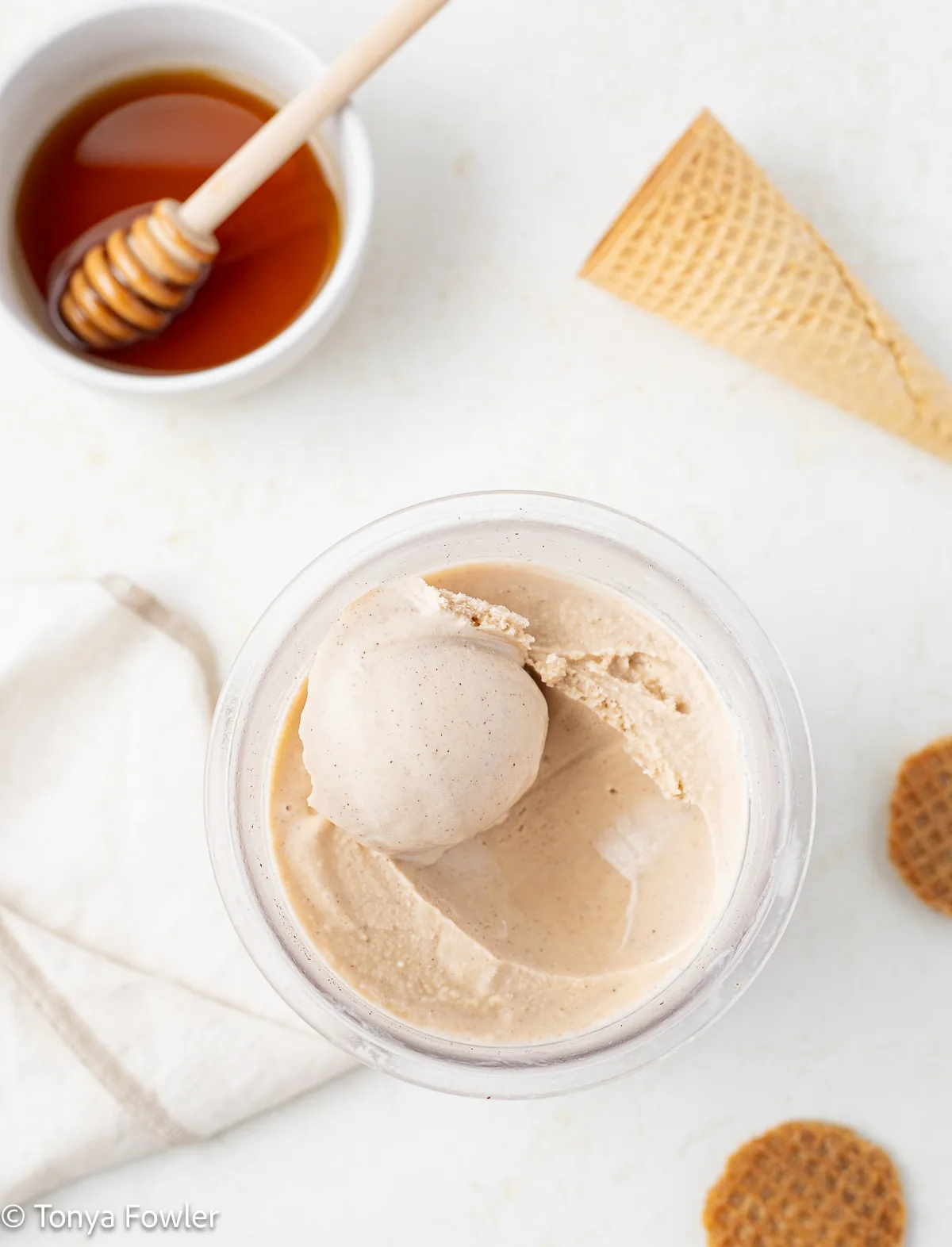 Scoop of honey ice cream in a pint container surrounded by honey and honey wafers.