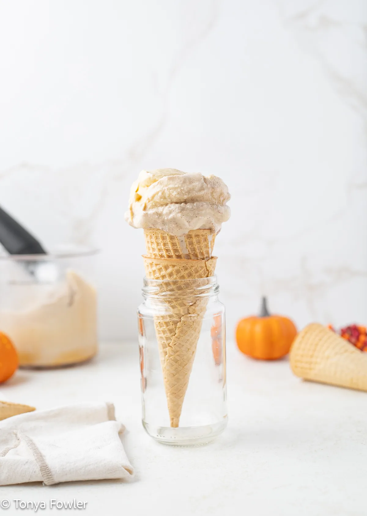 A scoop of pumpkin spice ice cream in an ice cream cone inside of a jar.
