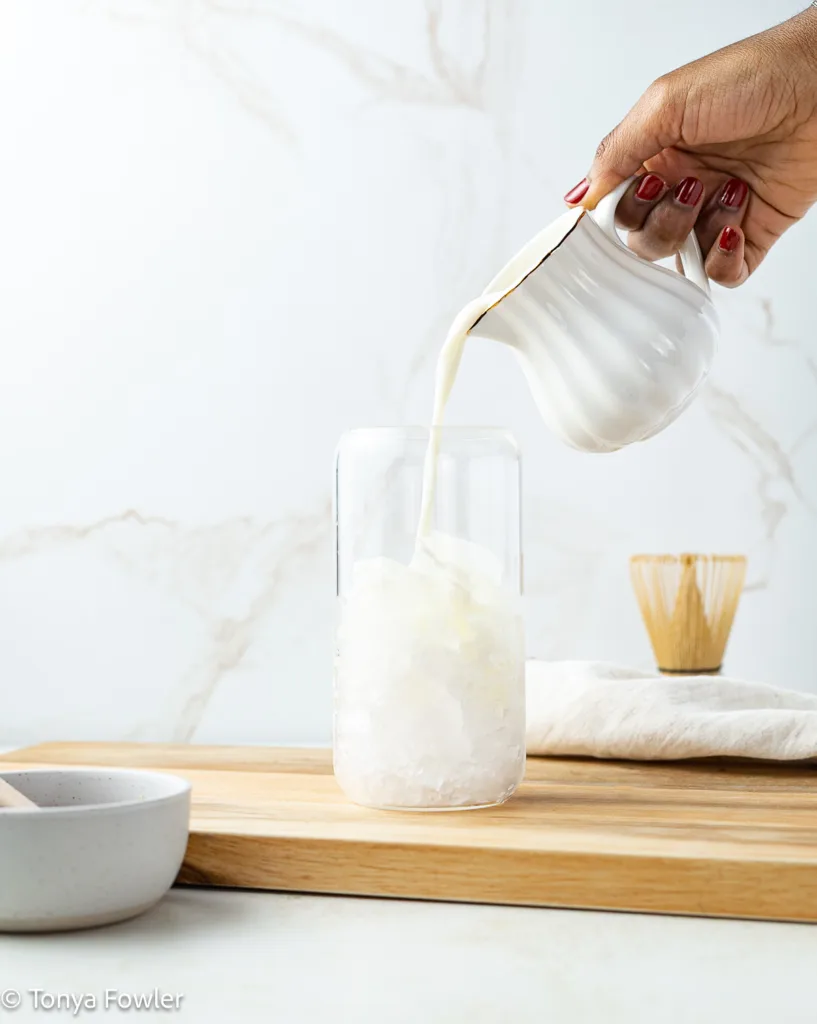 Milk being poured into a glass with ice.