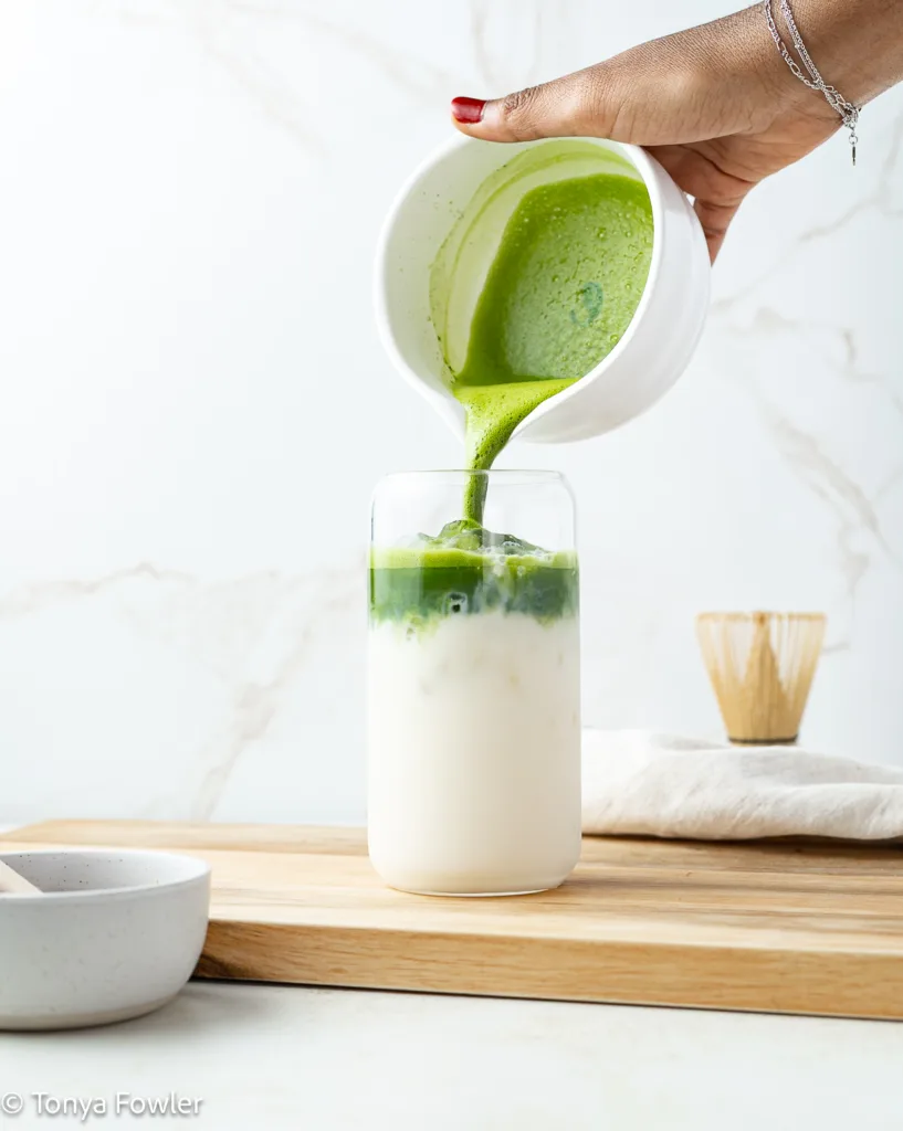 Matcha being poured into a glass with milk and ice.