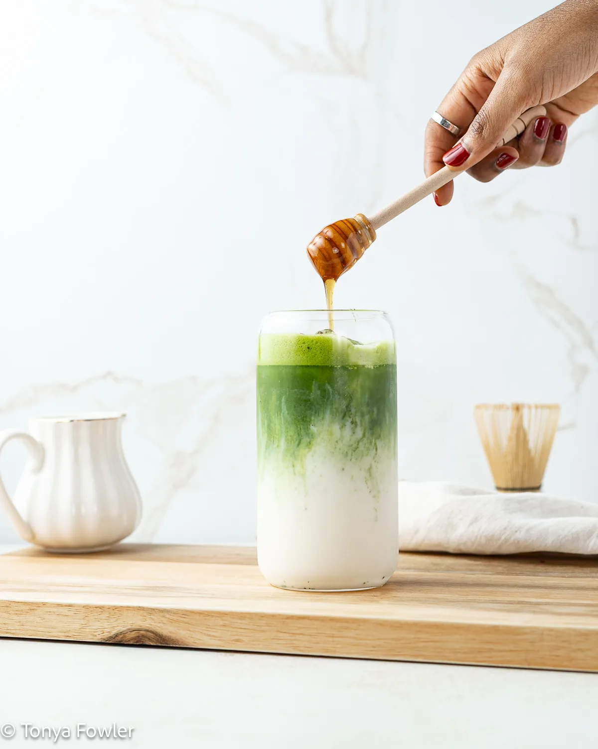 A honey dipper drizzling honey over a matcha latte.