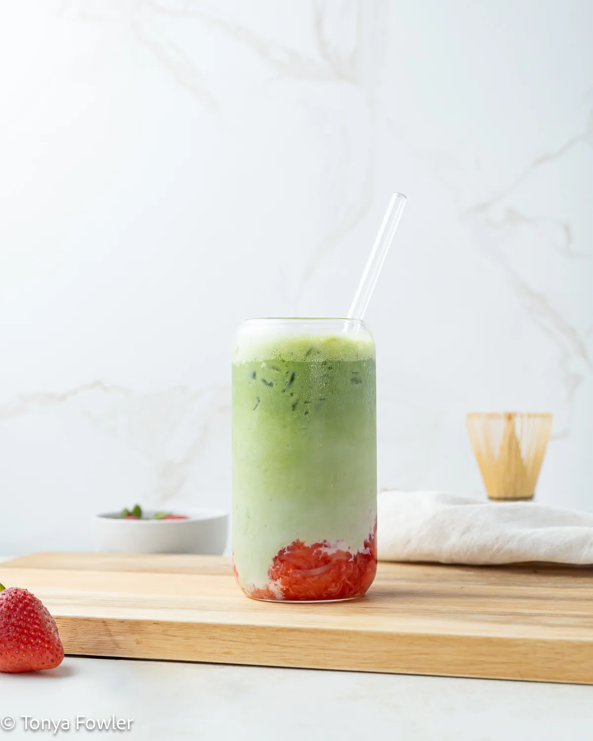 Strawberry protein matcha latte in a glass sitting on a cutting board.