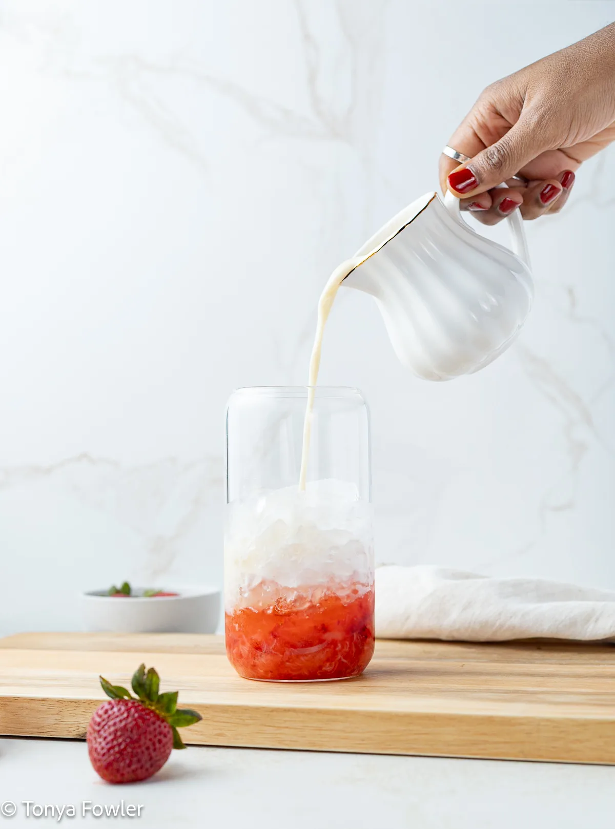 Milk being poured into a glass with ice and strawberries.