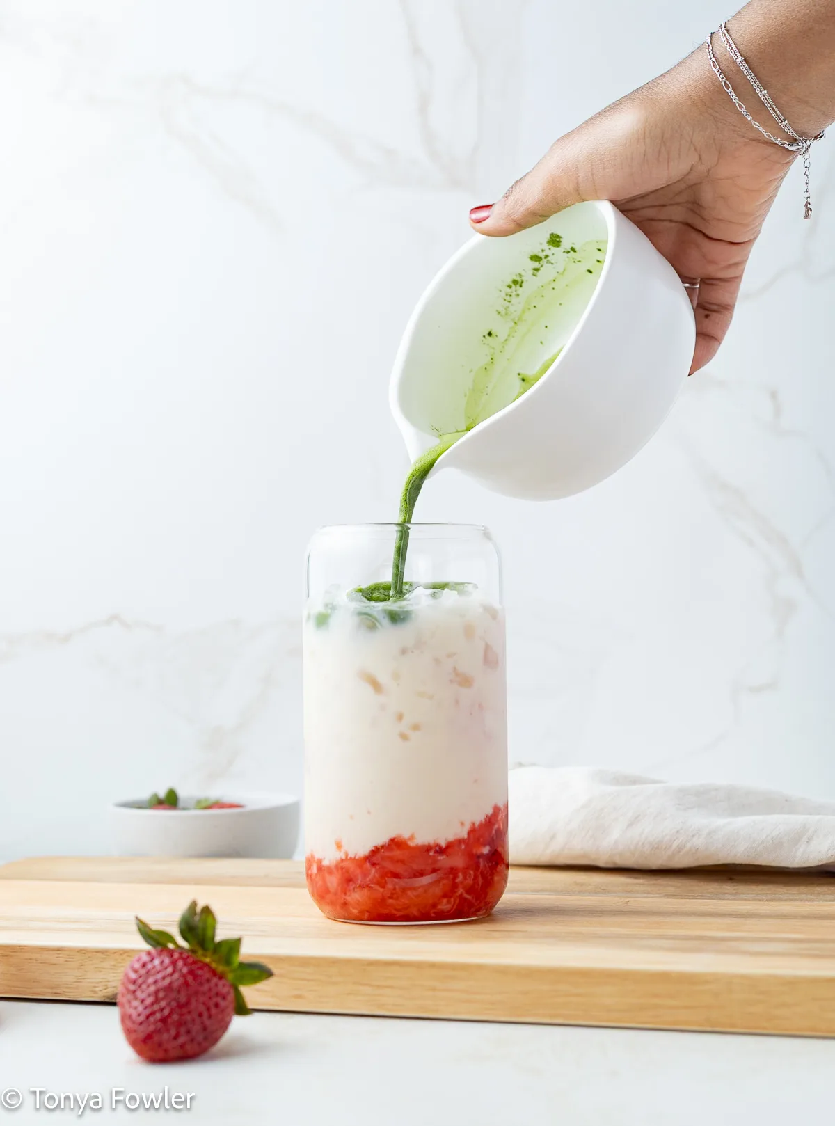 Matcha being poured into a glass with milk and strawberries.