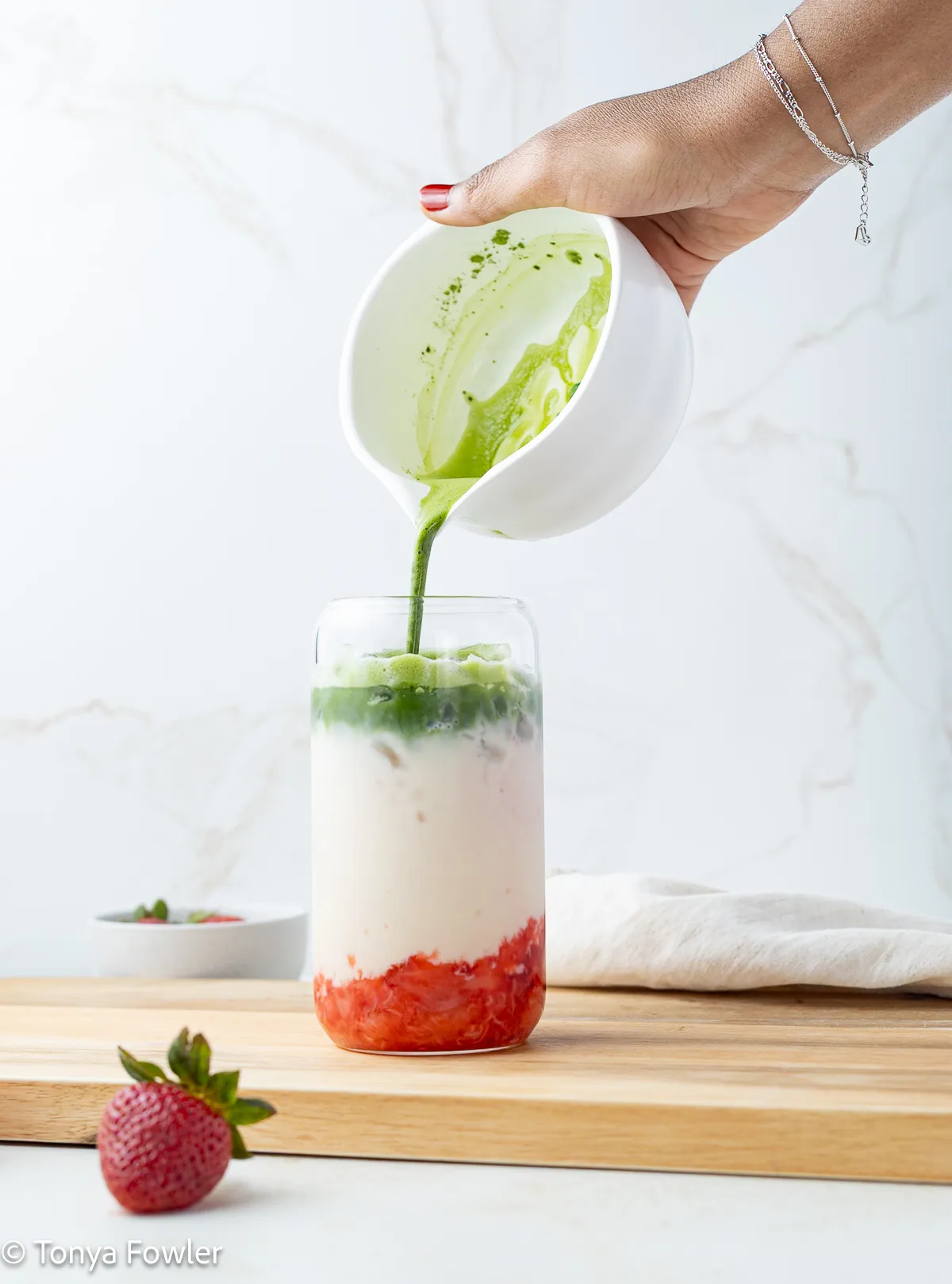 Hand pouring matcha into a glass with milk and strawberries.