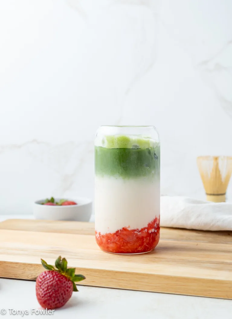 A strawberry protein matcha latte in a glass sitting on a cutting board.