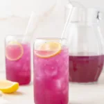 Butterfly pea flower lemonade in a glass with slices of lemons.
