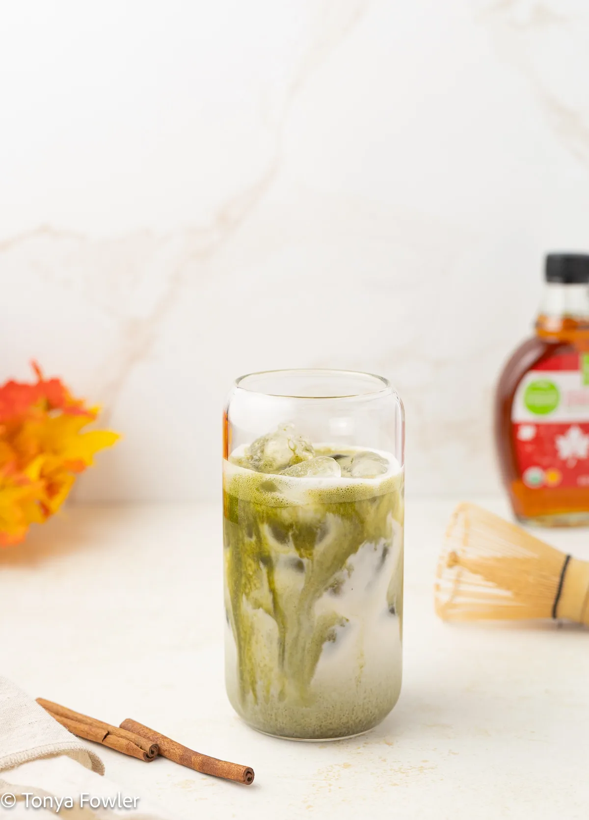 Matcha latte in a glass with cinnamon sticks on the table.