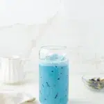 Butterfly pea flower latte in a glass with butterfly pea flower petals on a counter.